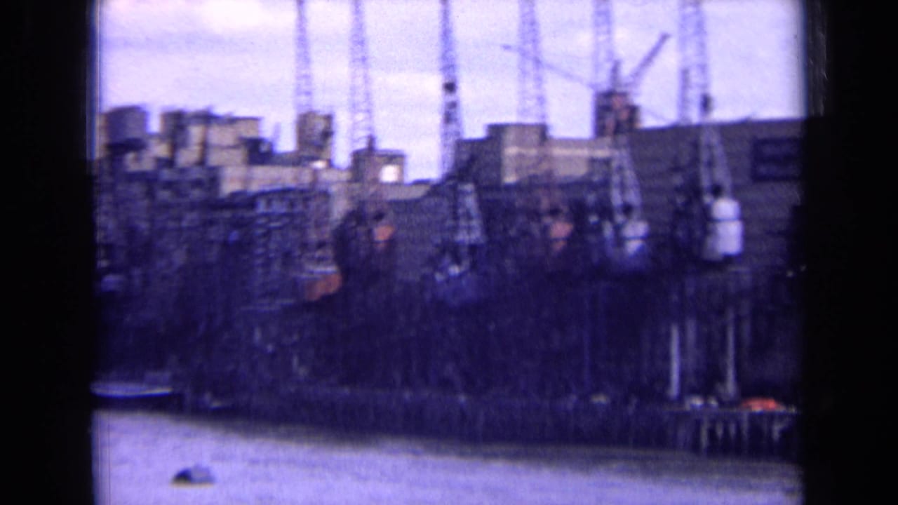 Soft 8mm frame showing an England industrial dock area with cranes, buildings, and river frontage in 1963.