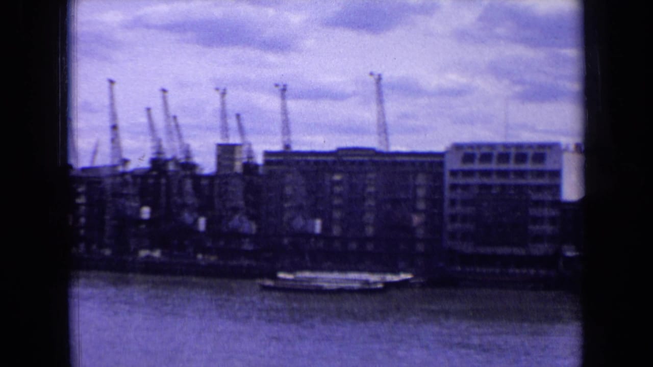 1963 England harbor view showing a long boat on the water before dockside buildings and tall cranes.