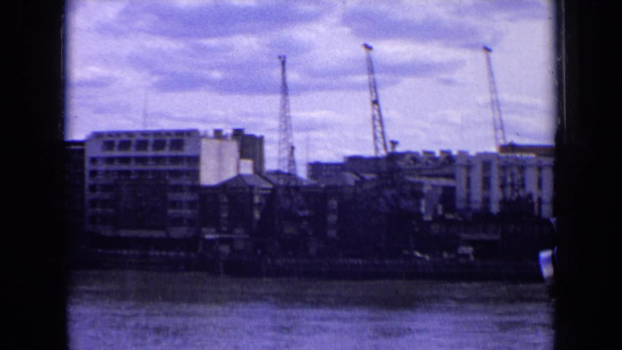 Riverside cranes and buildings viewed across water through dark frame edges.