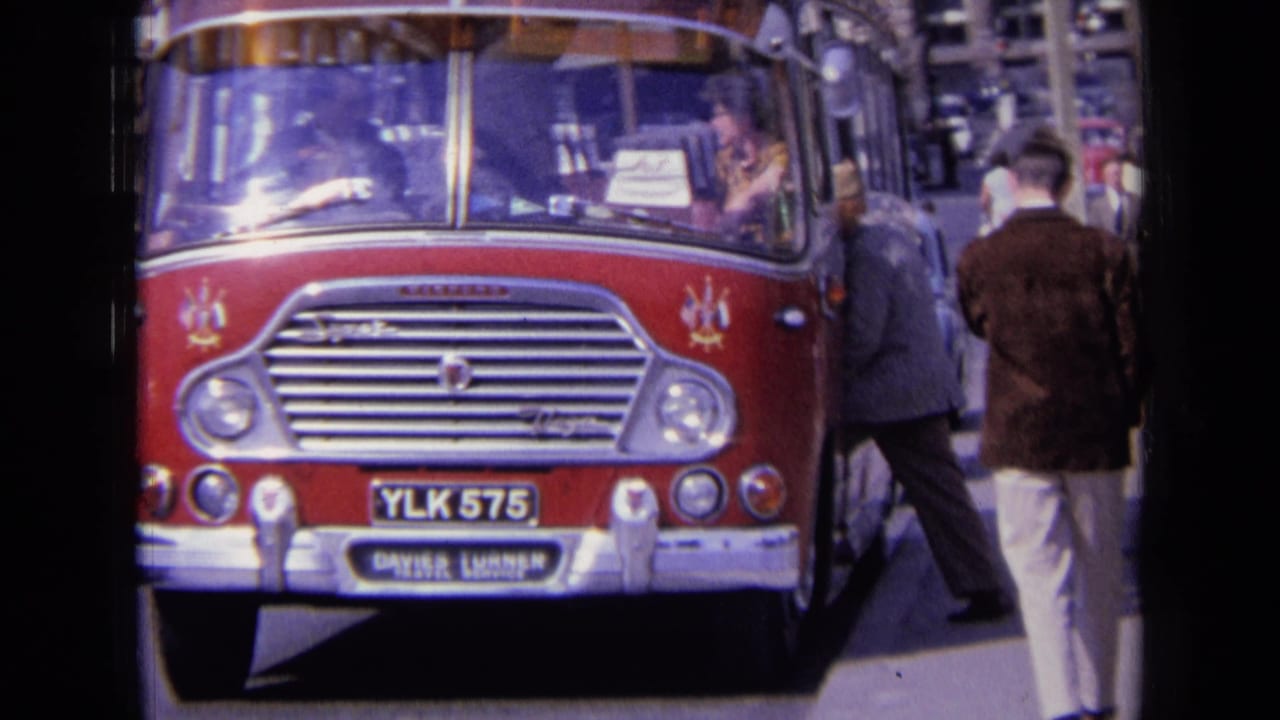 1963 England street view of a red bus marked YLK 575, with pedestrians beside it and period cars in the background.