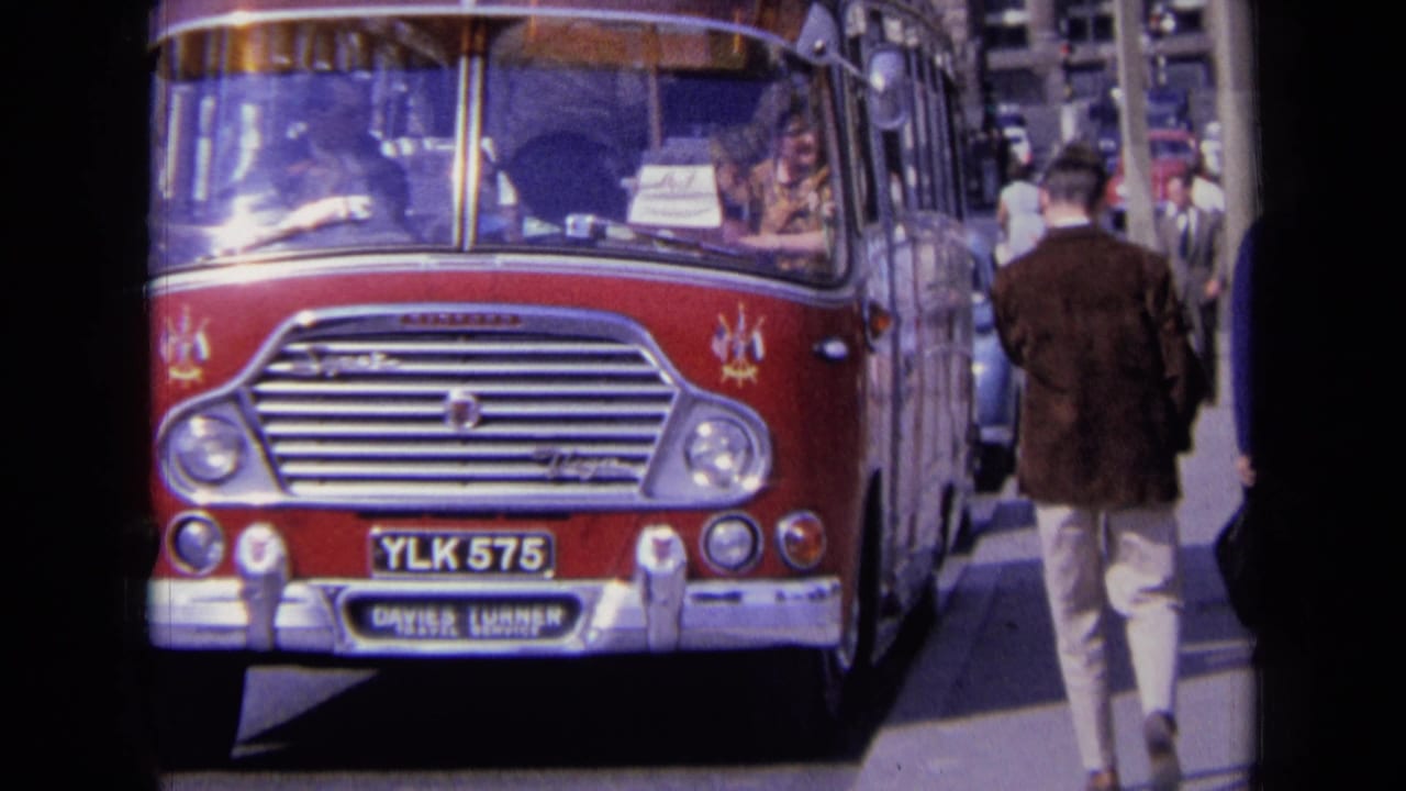 Red vintage bus facing the camera on a city street with pedestrians nearby.