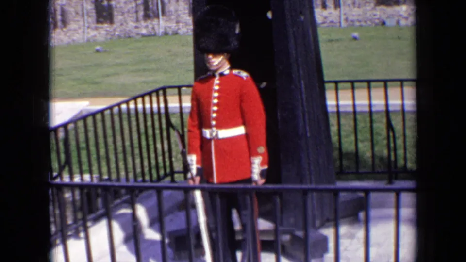 Visitor-shot 1963 England frame showing a British ceremonial guard at attention near a black sentry box and stone courtyard wall.