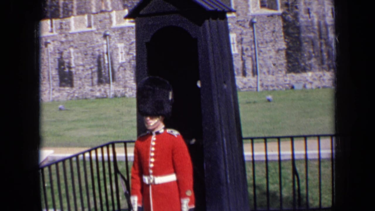 1963 England frame showing a ceremonial guard in red tunic and bearskin-style hat at a historic stone site.