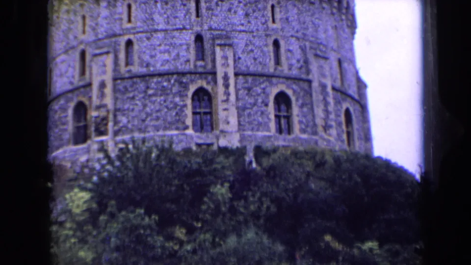 The round stone castle tower remains framed above trees, with crenellations and narrow arched windows visible.