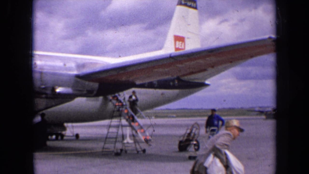 1963 England frame showing the rear of a BEA propeller plane, boarding stairs, ground equipment, and several people on the airport apron.