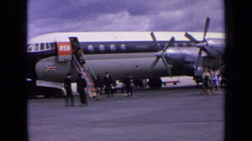 1963 England home-movie view of passengers and staff gathered near a BEA propeller aircraft as boarding stairs reach the forward door.