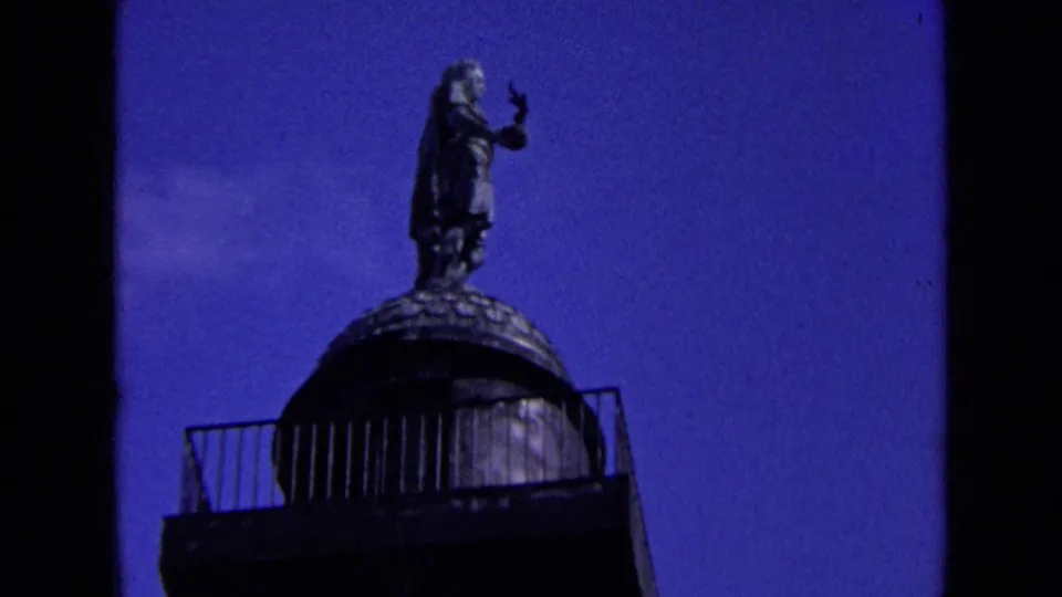 Low-angle 1963 England frame showing a statue above a column or monument against saturated blue sky.