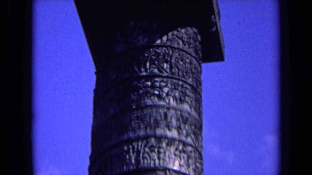 1963 England 8mm frame showing a weathered carved column shaft in close-up against saturated blue sky.