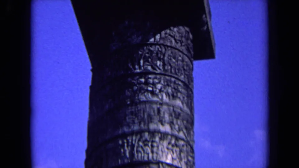 1963 England 8mm frame showing a weathered carved column shaft in close-up against saturated blue sky.