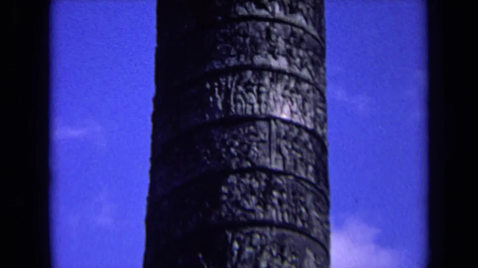 Close 8mm view of the column shaft, with carved horizontal bands and dark shadowed edges against sky.