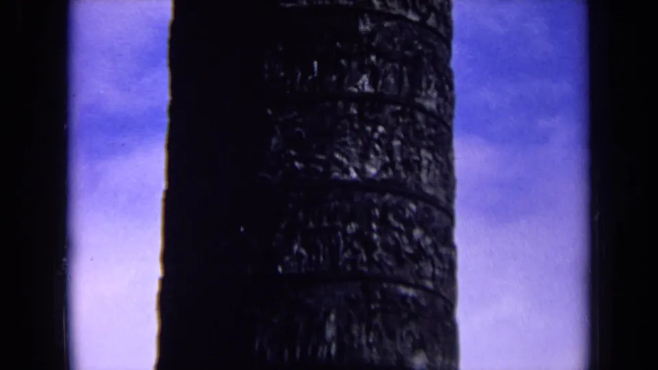 1963 England 8mm frame showing a close view of a dark carved column surface against a blue-tinted sky.