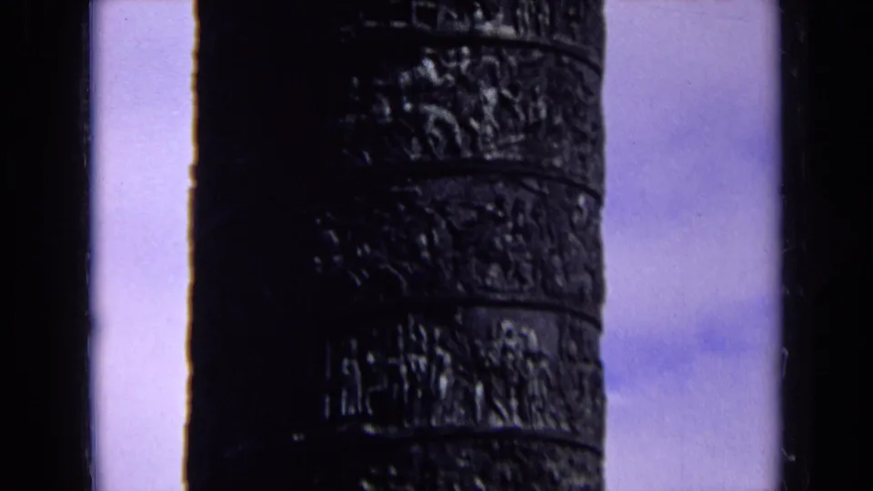 1963 England 8mm view of a dark banded column, its carved surface silhouetted against a blue-tinted sky.