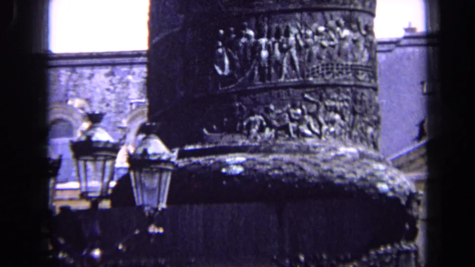 1963 England 8mm frame with the monument column centered, showing carved relief panels, lamps and nearby masonry details.