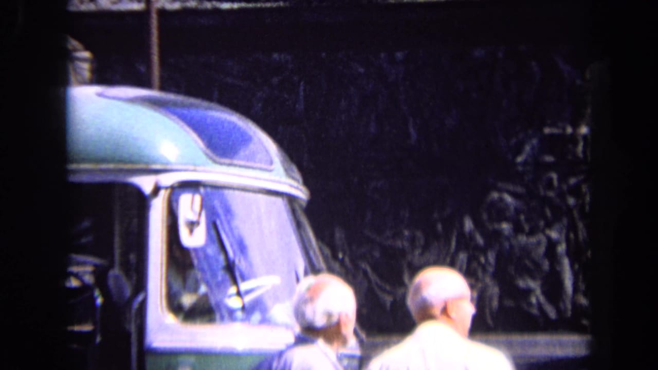 1963 travel footage frame showing two older men near a bus, with part of the Arc de Triomphe area visible behind them.
