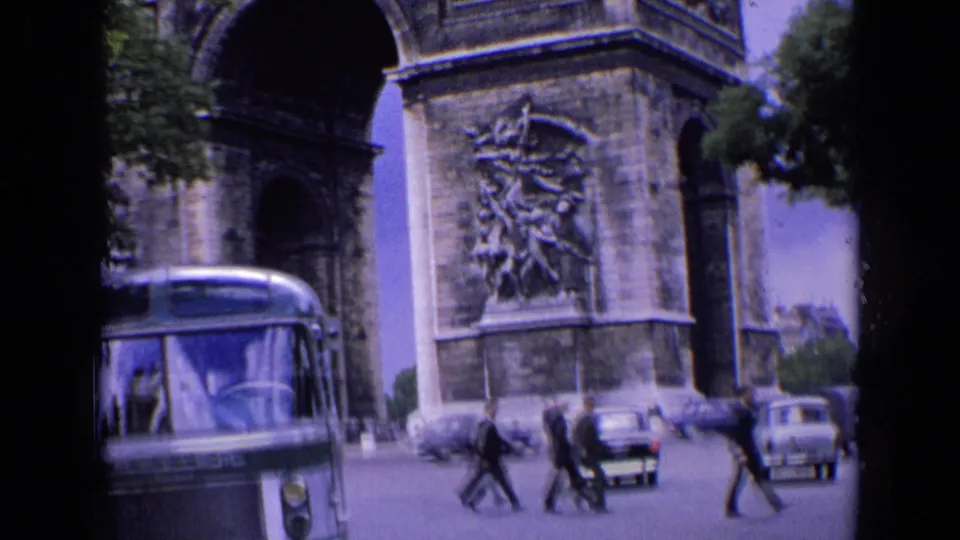 1963 Paris street view with the Arc de Triomphe, a green-and-white bus, pedestrians, and cars passing nearby.