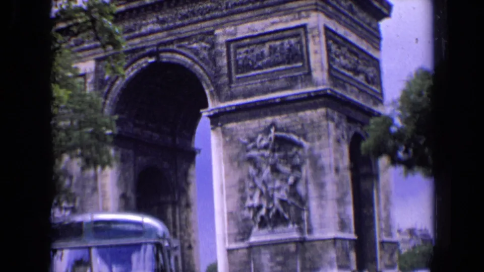 1963 Paris frame showing the Arc de Triomphe stone arch and reliefs above the roofline of a bus.