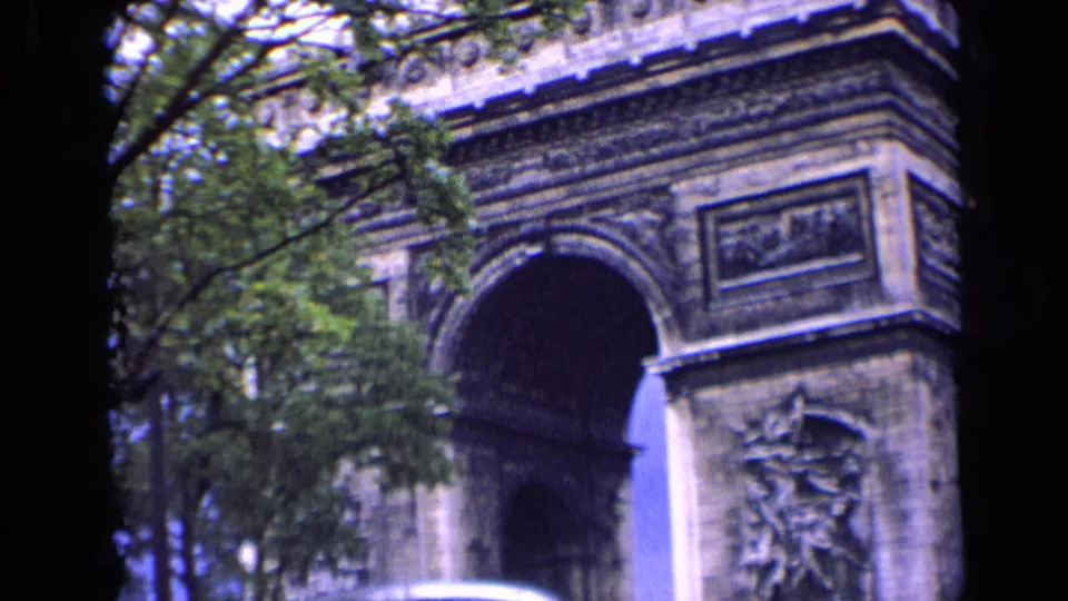 1963 Paris home-movie frame showing the Arc de Triomphe through trees, with soft focus and blue-shifted 8mm color.