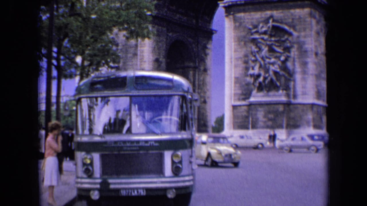 1963 Paris street view with a green-and-white bus, woman at the curb, passing cars, and the Arc de Triomphe behind.