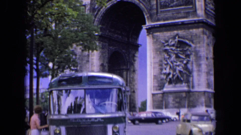 1963 France frame showing the bus at the curb with trees overhead and Arc de Triomphe stonework in the background.