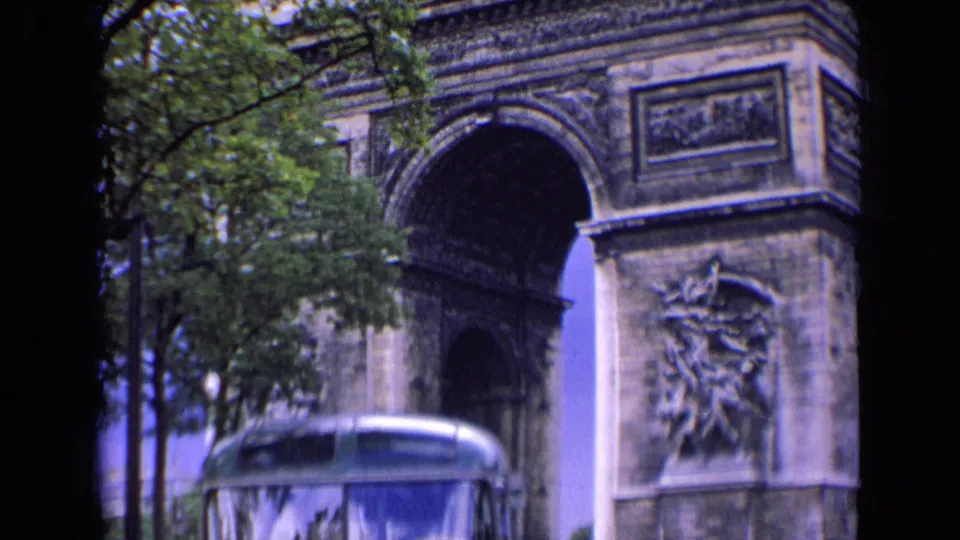 1963 Paris home-movie frame emphasizing the Arc de Triomphe above the parked bus and leafy street edge.