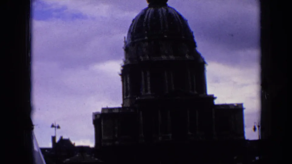 1963 France 8mm frame showing a dark silhouetted church dome with a cross-topped steeple beneath a purple-blue cloudy sky.