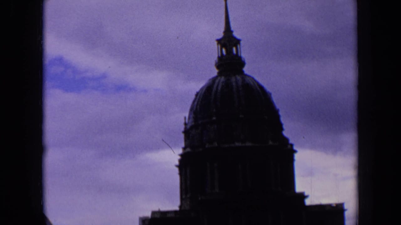 1963 France home-movie frame with a silhouetted church dome and slender steeple set against a moody clouded sky.