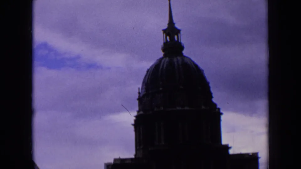 1963 France home-movie frame with a silhouetted church dome and slender steeple set against a moody clouded sky.