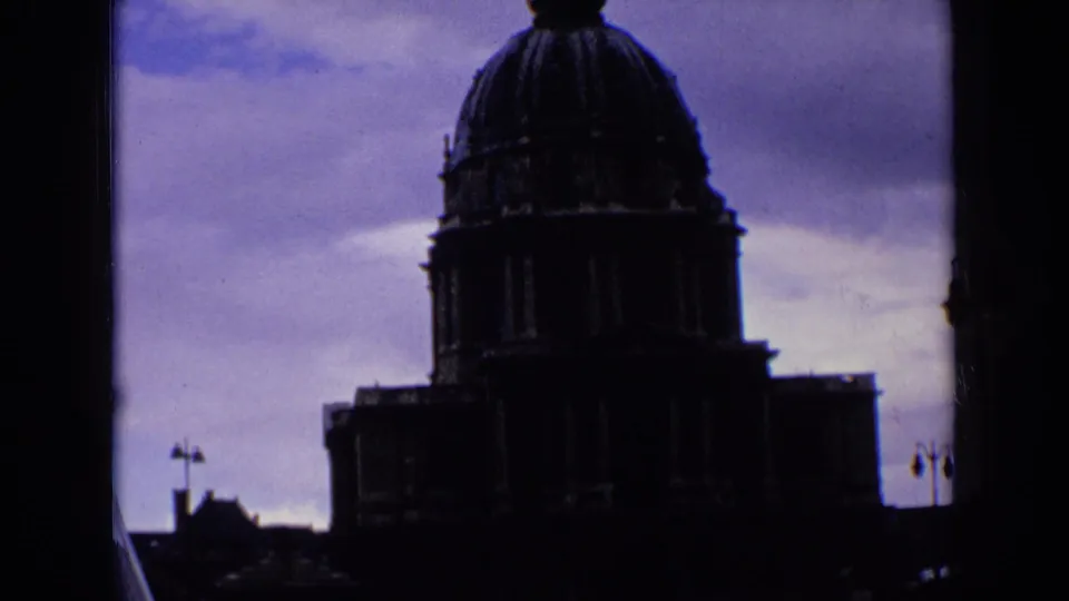 1963 8mm frame of a monumental French building in deep silhouette beneath a purple-blue sky.