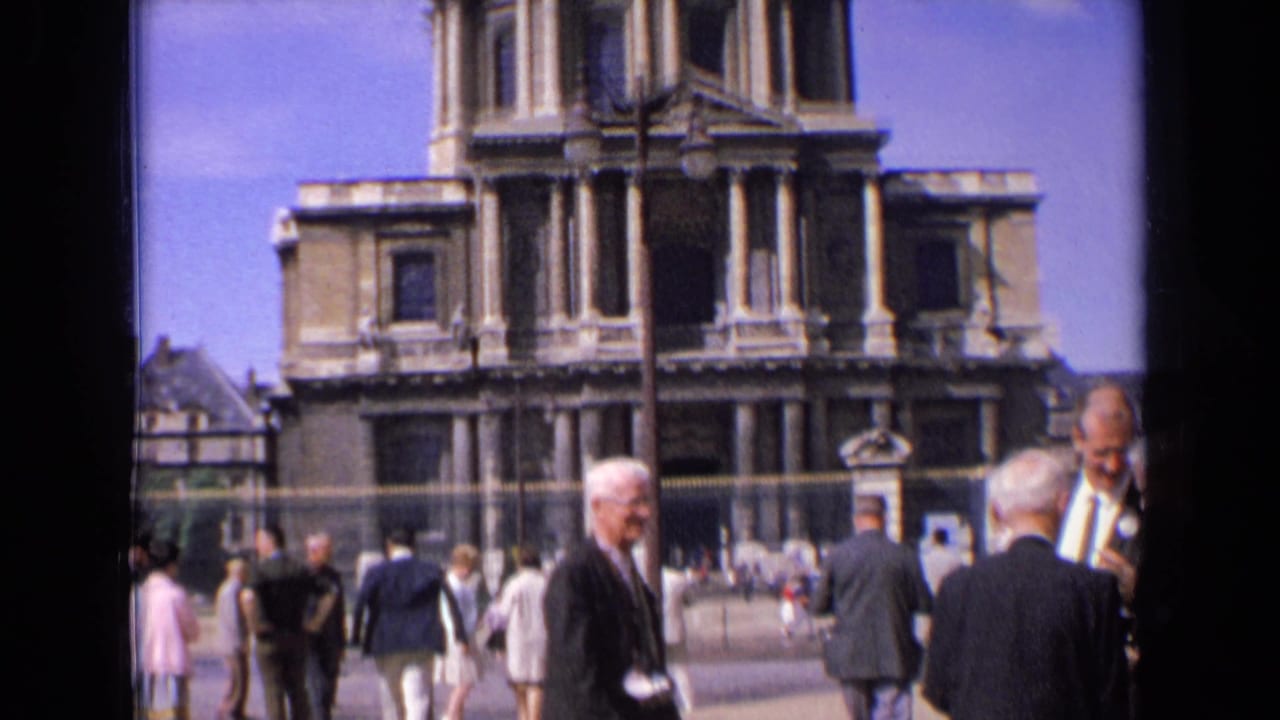Older men stand and walk before a domed stone cathedral facade.
