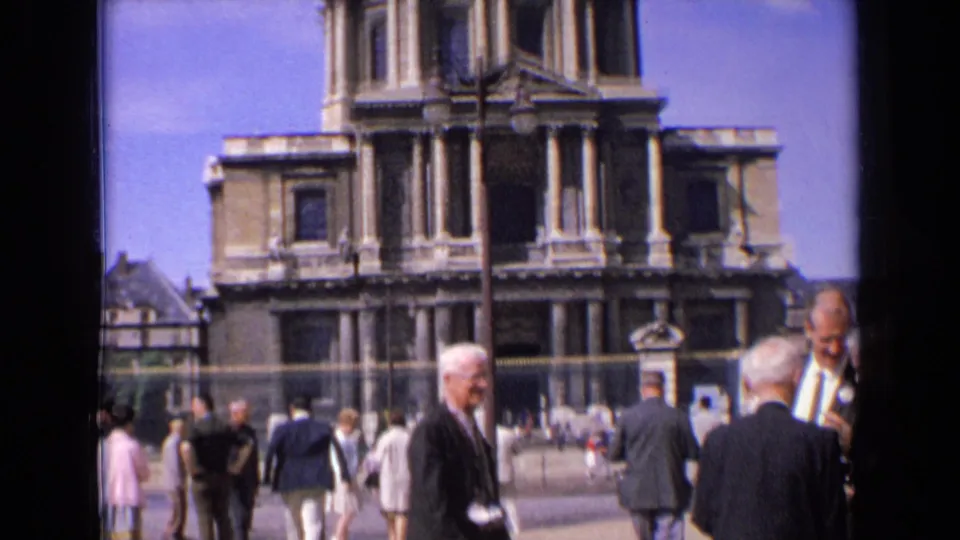 1963 France 8mm frame showing older men gathered near a grand stone cathedral or church facade under blue sky.