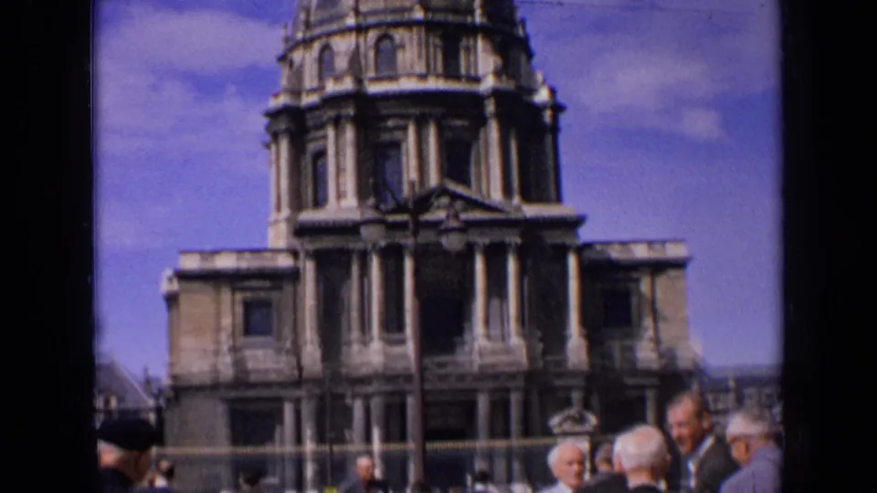 1963 France 8mm frame with older men in the foreground and a domed stone religious building behind them.