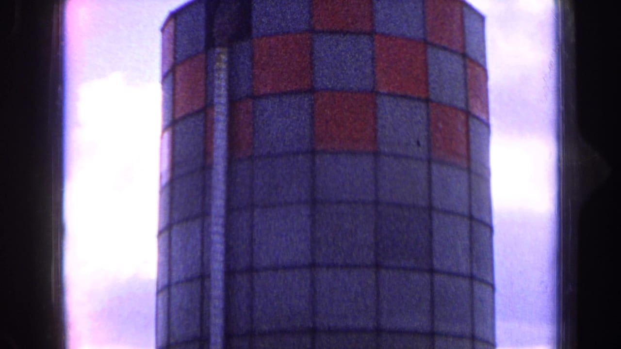 1963 France 8mm view of a tall cylindrical farm silo with red-and-gray checkered upper panels against clouds.