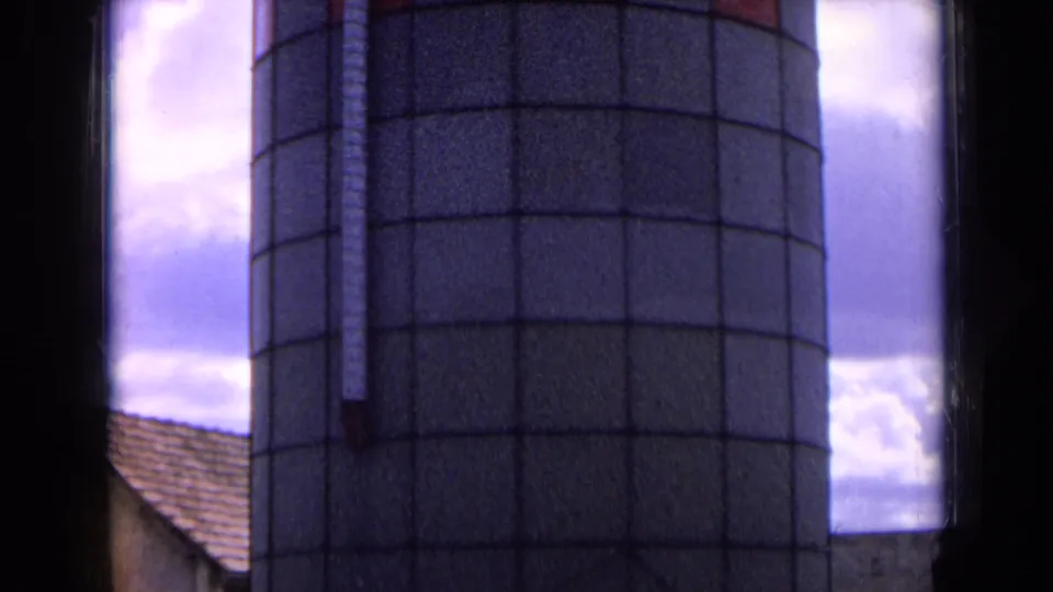 1963 France rural frame showing the lower section of a cylindrical silo, a tiled farm roof, and cloudy sky.