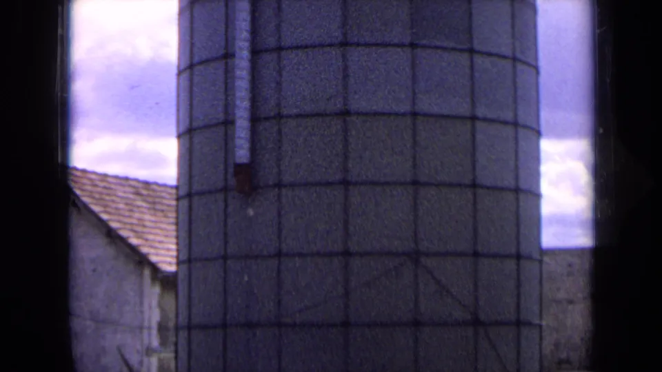 1963 France 8mm frame of a checkered farm silo rising above nearby roofs, bordered by dark film-edge shadows.