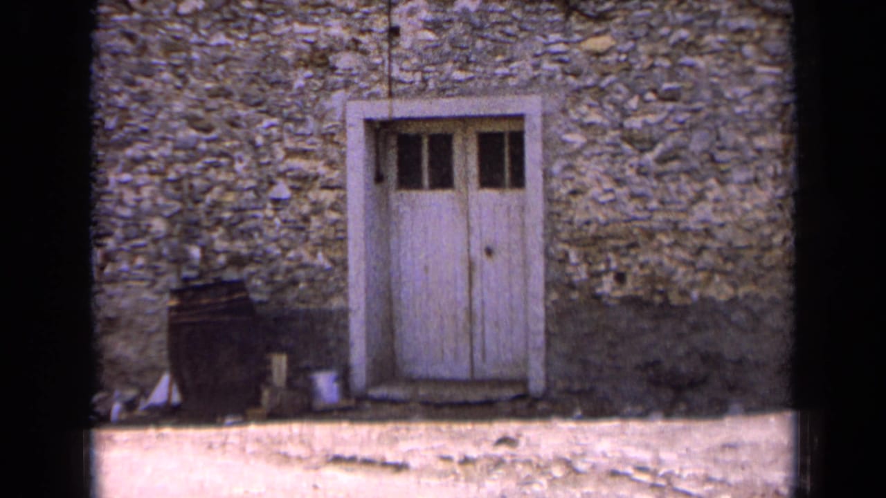 1963 France frame of a white paneled door in rough stone masonry, with a dark barrel beside it and pale ground below.