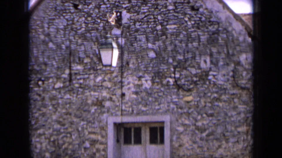 1963 France frame showing a lantern mounted above a white door on a rough stone house facade, with roofline and sky at the edges.