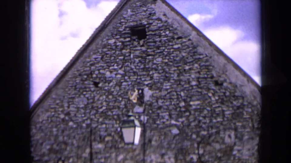 1963 France frame of a stone building gable with rough masonry, a small opening, and a lantern mounted near the center.