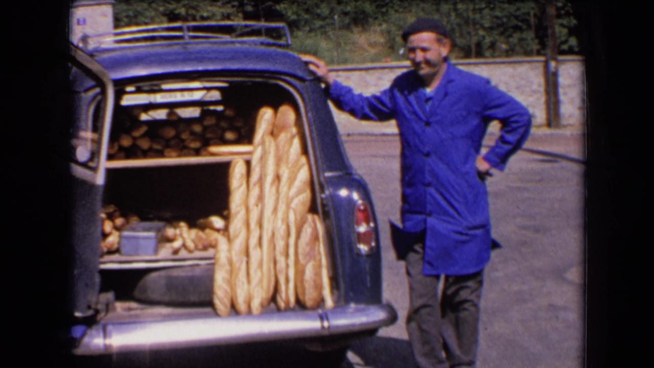 Baker rests one hand on the car while standing near an open trunk full of bread.