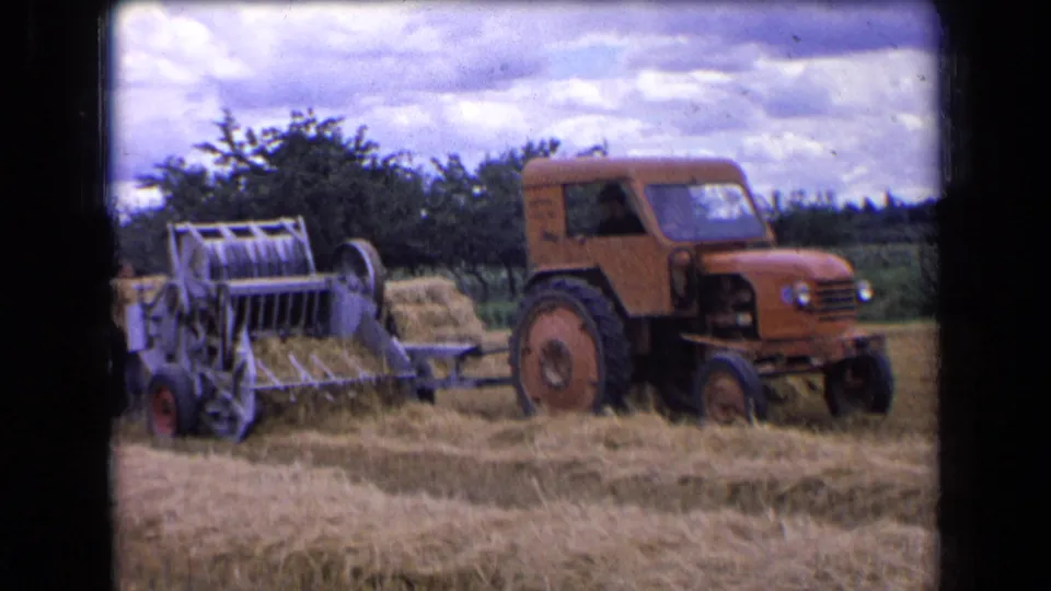 1963 rural France 8mm frame with the hay baler prominent as the tractor moves through a dry cut field.