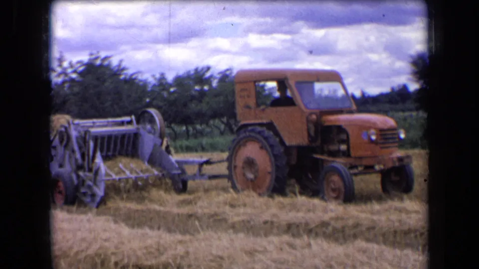 1963 rural France 8mm frame showing the tractor and baler from the side in a harvested hay field.
