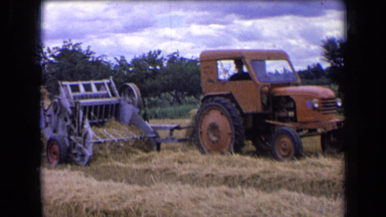 Orange tractor pulling a gray hay baler through a cut field.
