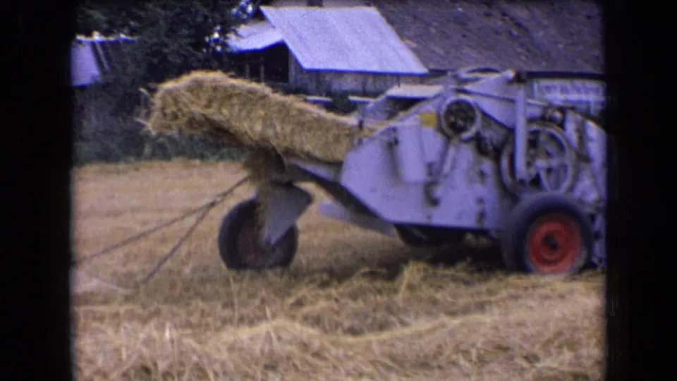 1963 France 8mm frame showing a white hay or straw baler from the side, loaded with straw in a cut field.