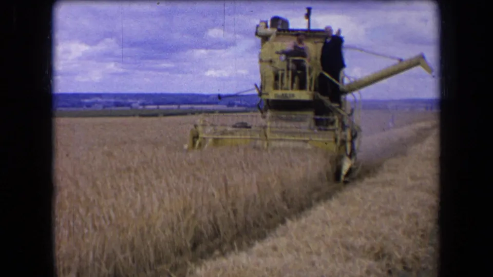 1963 France 8mm frame showing a yellow combine harvester cutting wheat, with adult workers visible on the machine.