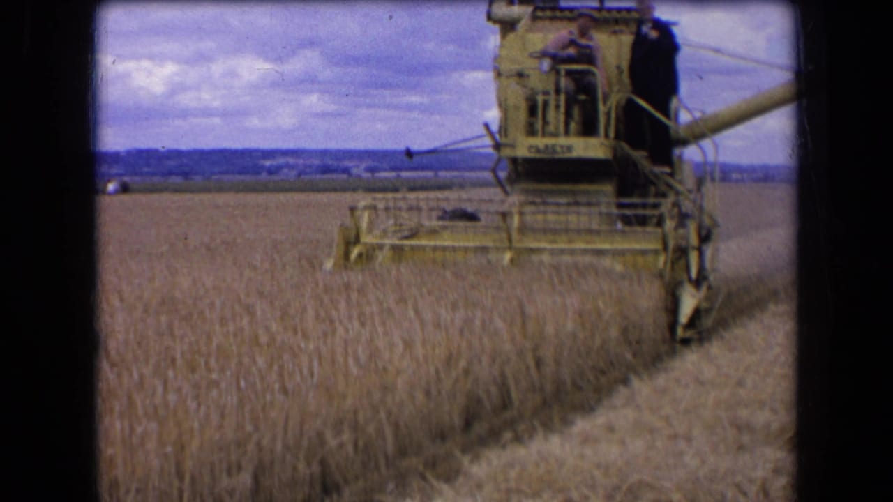 1963 France 8mm frame showing a yellow combine moving across a wheat field with men visible on the operator platform.