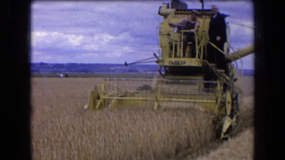 1963 France 8mm frame with the yellow combine close to camera, cutting wheat as two men ride on the platform.