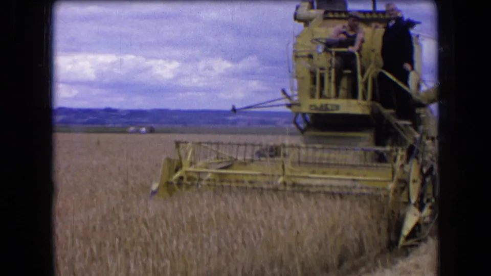 1963 France 8mm frame showing a yellow Claas combine partly in view as it harvests wheat, with two men on the machine.
