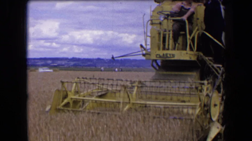 A closer 8mm view shows the combine header and open operator area during a 1963 wheat harvest in rural France.