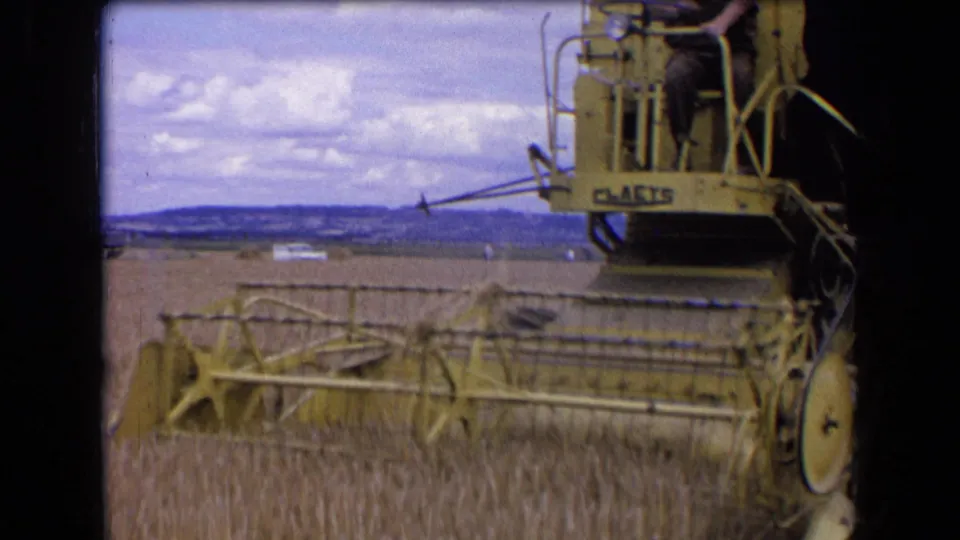 The combine is framed from the side as it harvests wheat, with Claas lettering visible and a broad rural horizon behind it.
