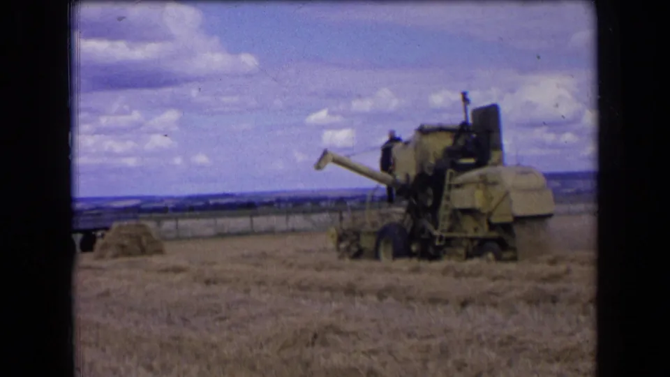 A 1960s farm machine, identified in metadata as a Claas combine, works in a French wheat field with a person aboard.