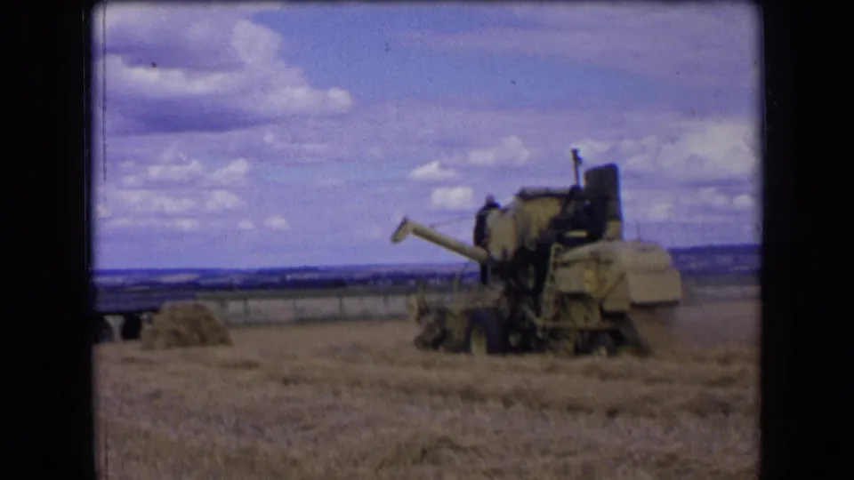 The combine harvester continues through the field, with wheat stubble in front and open countryside behind it.